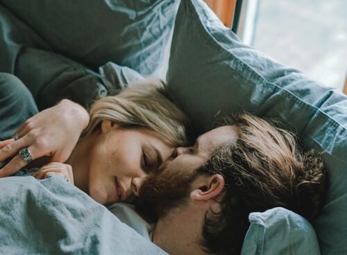 man kissing woman's forehead while lying on bed