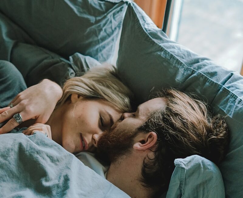 man kissing woman's forehead while lying on bed
