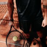 person in black shorts holding green tennis racket