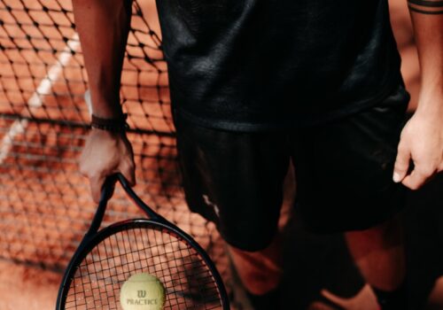 person in black shorts holding green tennis racket
