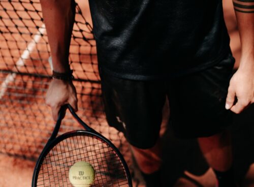 person in black shorts holding green tennis racket