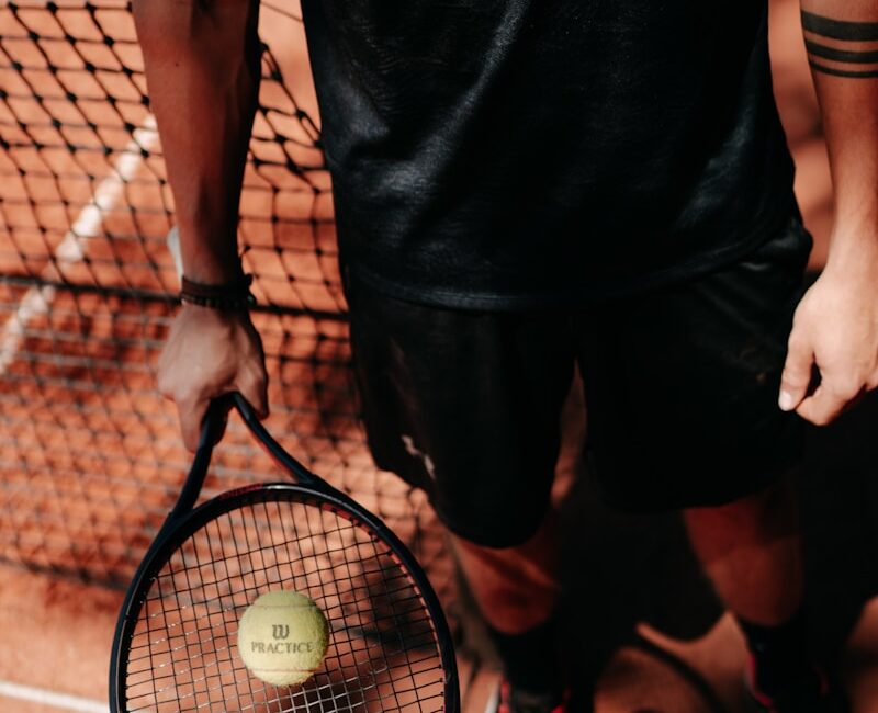 person in black shorts holding green tennis racket