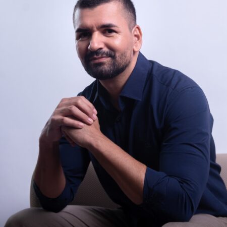 Man sitting on a couch with hands clasped.